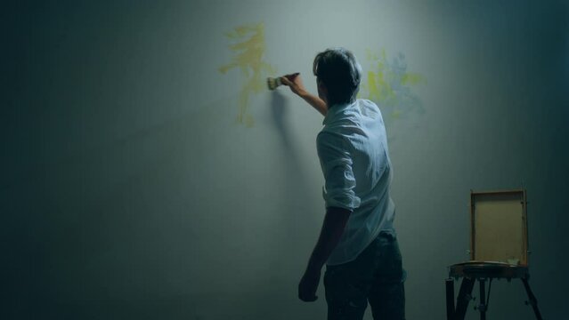 Concept of modern artwork artist man doing a contemporary painting on the big wall using paint brush and oil colour