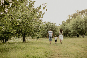 Fototapeta premium A happy family with a child walking in the park. Rear view: a young father holding the hand of his wife and young son. Family outdoor recreation