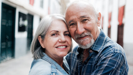 Happy multiracial senior couple hugging each other with city on background - Elderly people relationship family concept