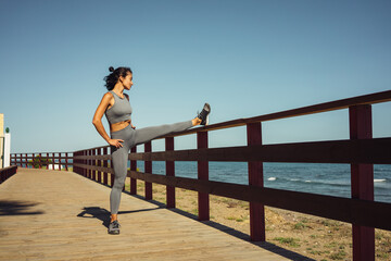 a beautiful brunette girl in gray leggings is warming up before running on the seashore