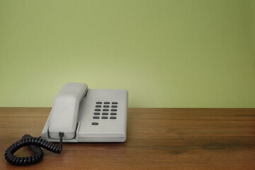 Grey retro style telephone with green background on wooden desk