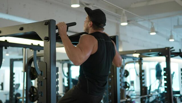 Natural fitness man pumping up muscle doing pull-ups exercises in gym. Handsome strong athletic caucasian male doing back muscles workout at fitness center - perspective view slow motion