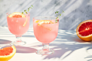 A chilled drink with grapefruit or red orange in glasses on a gray background under the shadow of palm leaves. Summer soft drinks and cocktails with fresh fruit