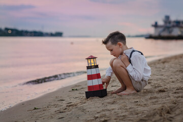 A boy on the coast holds a toy litlle lighthouse in his hands. Dreams of a child about the sea. A...