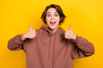 Photo of adorable overjoyed lady showing thumb up gesture both arms agree wear brown hood shirt...