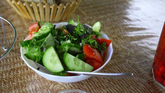 Vegetable salad with cucumber, tomato, onion and green salad. Close-up photo of healthy food on table in restaurant or cafe, next to it is bread and decanter of cornel compote.