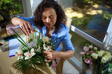 Inspired woman, florist, event manager putting a greeting card in a floral arrangement in the...