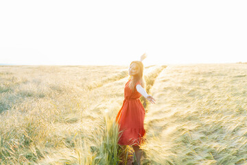A happy young woman with raised arms relaxing in wheat field on sunset. Celebrating freedom....