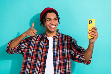 Photo of satisfied guy with cornrows dressed checkered shirt doing selfie on smartphone show thumb...