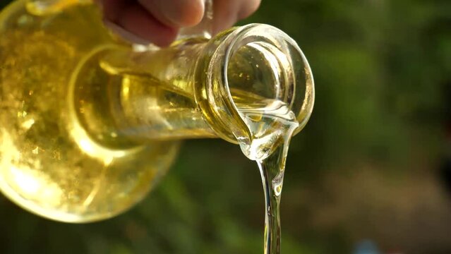 slow motion shot of extra virgin olive oil being poured from a clear glass bottle