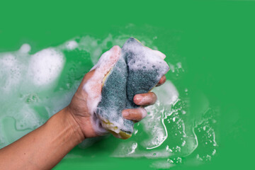 hand holding a foaming sponge from dish cleaner on a green background