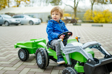 Adorable toddler boy riding his toy tractor in a city on sunny autumn evening. Young child riding a...