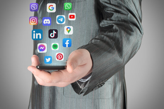 Businessman holding smart phone from which flying social media apps icons, on grey background, social media in smart phone concept
