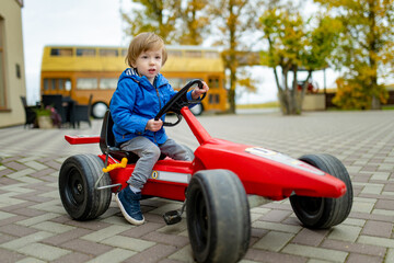 Adorable toddler boy riding his toy race car in a city on sunny autumn evening. Young child riding a roller.