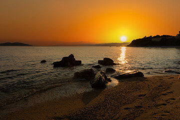 Sand beach with rocks on evening sunset. Beautiful colors and amazing sun in Greece