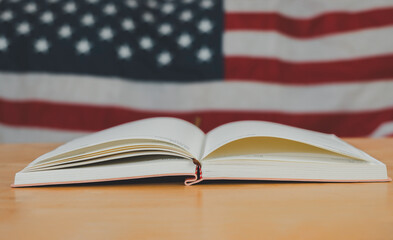 A simple composition of many books, stack or pile of books on wooden table with United States of America flag. One of them open with copy space.