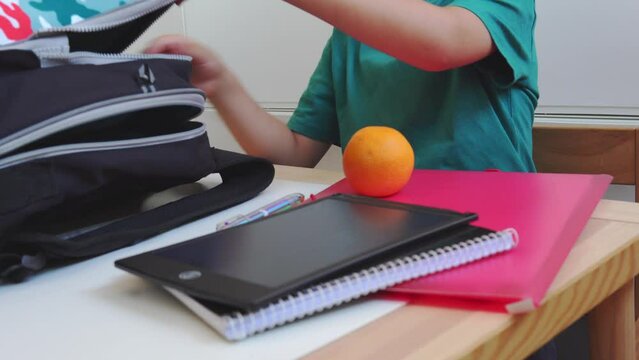 Kid preparing backpack in a  to go to school. Unrecognizable young boy keeping school supplies and fruit into his backpack