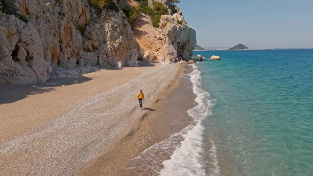 Aerial drone view woman traveler walking alone by Empty Wild secret beach in bay close to Antalya. Sandy beach and clear turquoise waters in Mediterranean Sea. nature of Turkey.