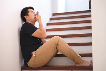 Sick Asian young man using inhaler to treat asthma and respiratory diseases at home. Asthma attack. Concept of allergy care.