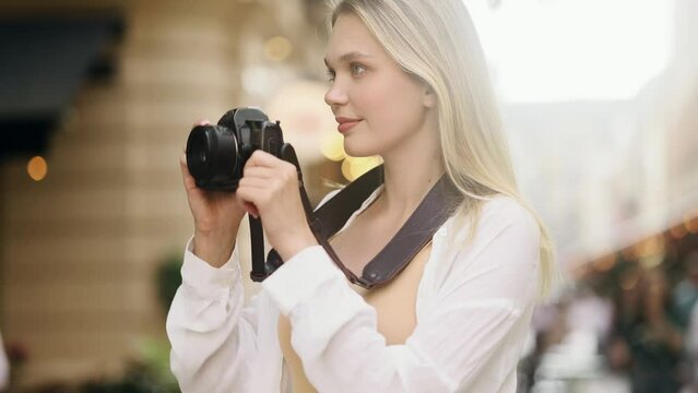 Portrait of pretty young blond woman photographer hold digital camera and looking around at urban city Charming tourist female taking pictures and enjoying beautiful day outdoors