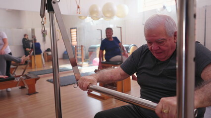 Elderly person exercising in Pilates Studio Group Session. One Older Caucasian man taking care of body by using machine