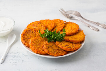 Carrot fritters with sour cream and greens on a white plate on a light blue background