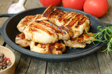Chicken or turkey thigh fillet steak on an old rustic table with tomatoes and other spices. Side view.