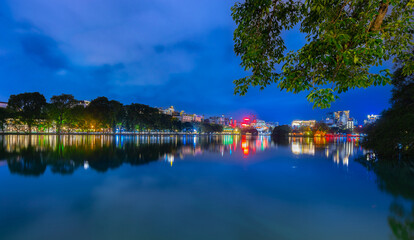 Obraz premium Hanoi City Old Quarters Lake at night glowing with vibrant colourful city lights surrounded by old historic buildings small bridge crossing the lake into a temple on a small island Hanoi Vietnam