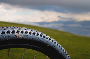 mountain bike tire with spikes close-up, with blurred background of green mountain fields and...