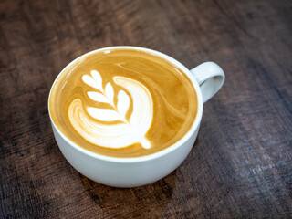 A cup of coffee with latte art. Black coffee with milk, called as Latte, with milky art on top, in white cup, on black wooden table