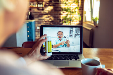 Senior woman on a video call with her doctor on the laptop in the kitchen