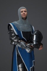 Royal guard dressed in medieval armor and blue surcoat, with chain mail coif, standing holding...