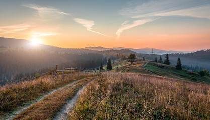 Mountain autumn landscape. Grassy road to the mountains hills during sunset. Nature background