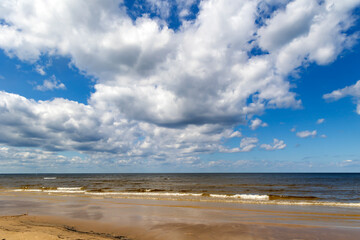 White clouds on blue sky over calm Baltic sea with sunlight reflection in sea. Nature shot in Latvia. The Latvian Coast of the Baltic Sea.