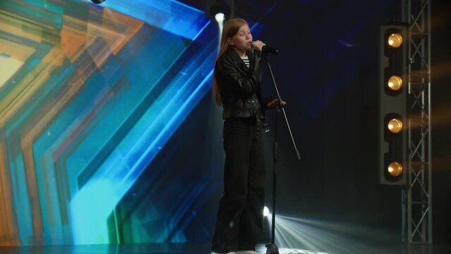 Young teenager girl singer performing on stage, contestant singing during recording of television style broadcast talent show