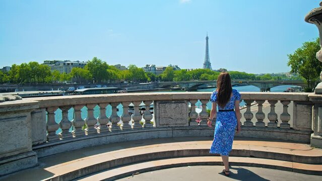 A beautiful woman in a dress walks on Pont Alexandre III bridge to look at the Tour in Paris, France. Arched bridge in a Beaux-Arts style, named after a Russian czar.
