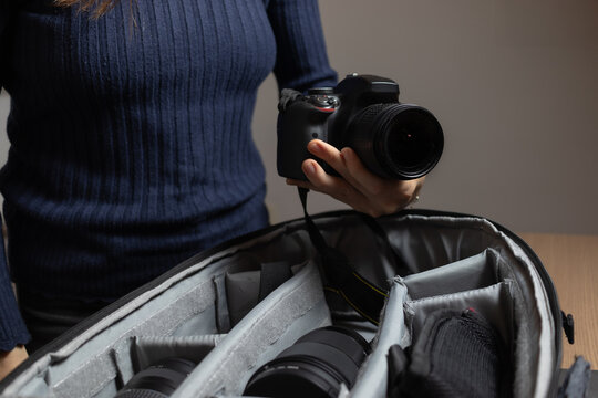 Young woman holds her professional photo camera while keeping photography items inside her backpack.