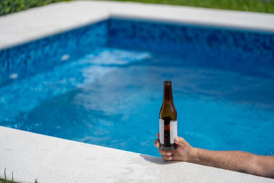 mano sosteniendo Botella de cerveza a un lado de la alberca en un día de verano