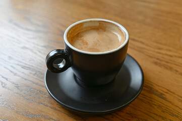 A black coffee cup with espresso coffee stands on a wooden table. close-up