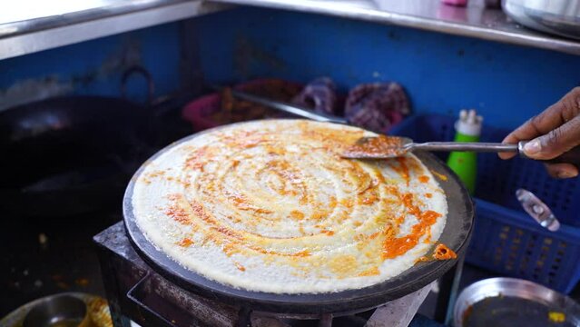 Spreading hot chili and other spices on famous Indian food dosa while making dosa on a hot gas stove, slow motion stock footage