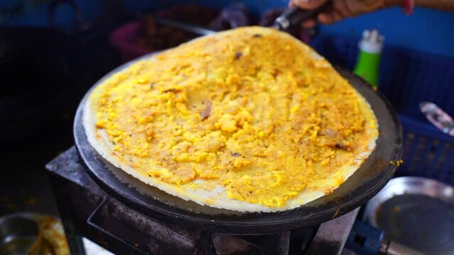 Spreading hot chili potato stuff and other spices on famous Indian food dosa while making dosa on a hot gas stove, slow motion stock footage