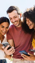 Young group of happy people smiling while using cell phone together. Smiling multiracial friends standing outdoors in the park holding smartphone devices. Technology, youth and social media concept