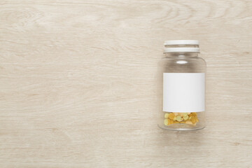 Plastic bottle with vitamins on wooden background, top view