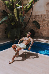 Fototapeta na wymiar Chico tatuado y musculoso posando en piscina estilo boho de hotel en un día de verano