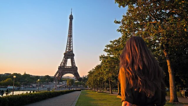 A beautiful woman in a dress looking at the romantic city of Paris, France. Female tourist visiting the historical Tower and enjoying the view of a golden sunset.