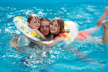 a young father in an embrace with his children daughter and son swims in the pool