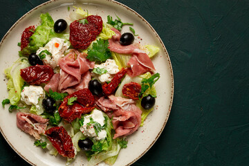 salad with dried tomatoes, prosciutto, soft cheese, olives, homemade, top view,