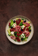 salad with dried tomatoes, prosciutto, soft cheese, olives, homemade, top view,