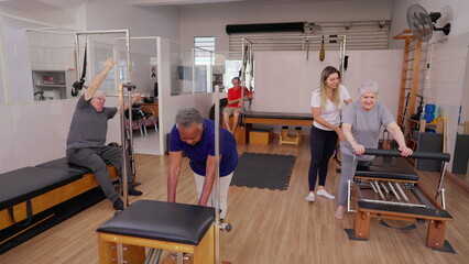Pilates Group Session of Seniors Exercising Together with the help of instructor coach orienting them to use machines