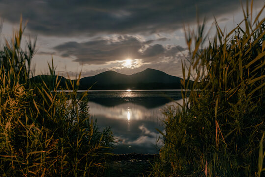 vue de deux sommets de montagnes sur la rive oppos&eacute;e d'un lac calme la nuit avec la lune dans le ciel bien centr&eacute;e entre les deux monts